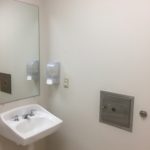 A bathroom with a mirror, sink and a wall mounted light.