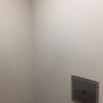 A white wall with a metal square in the corner.