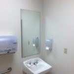 A bathroom with a mirror, sink and paper towel dispenser.