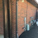 A brick wall with pipes and wires on the side.