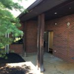 A brick building with a porch and trees in the background.