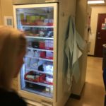 A woman looking in the refrigerator of an office.