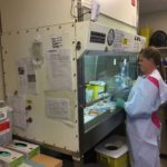 A person in white lab coat standing next to an open cabinet.